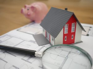 Table with magnifying glass with little home and piggy bank